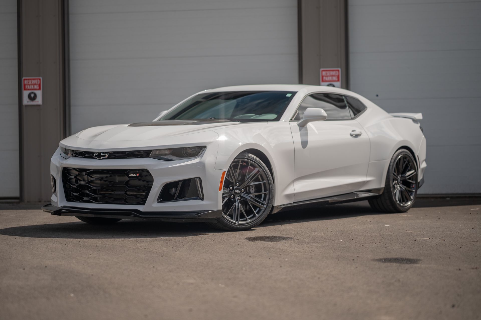 White sports coupe parked in front of garage doors, angled front view