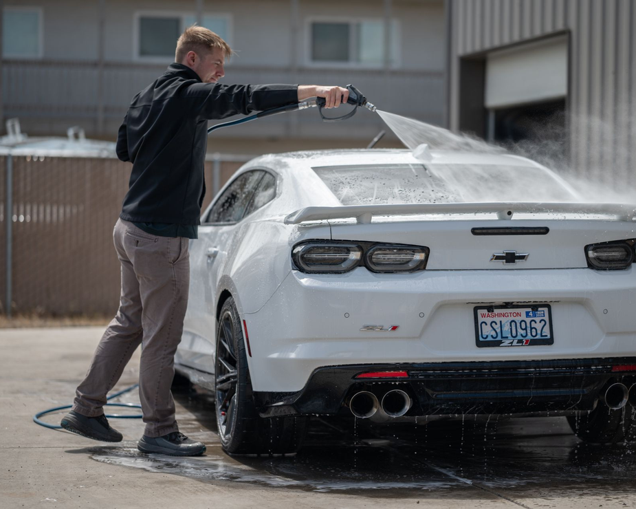Person rinsing a white sports car at a car wash