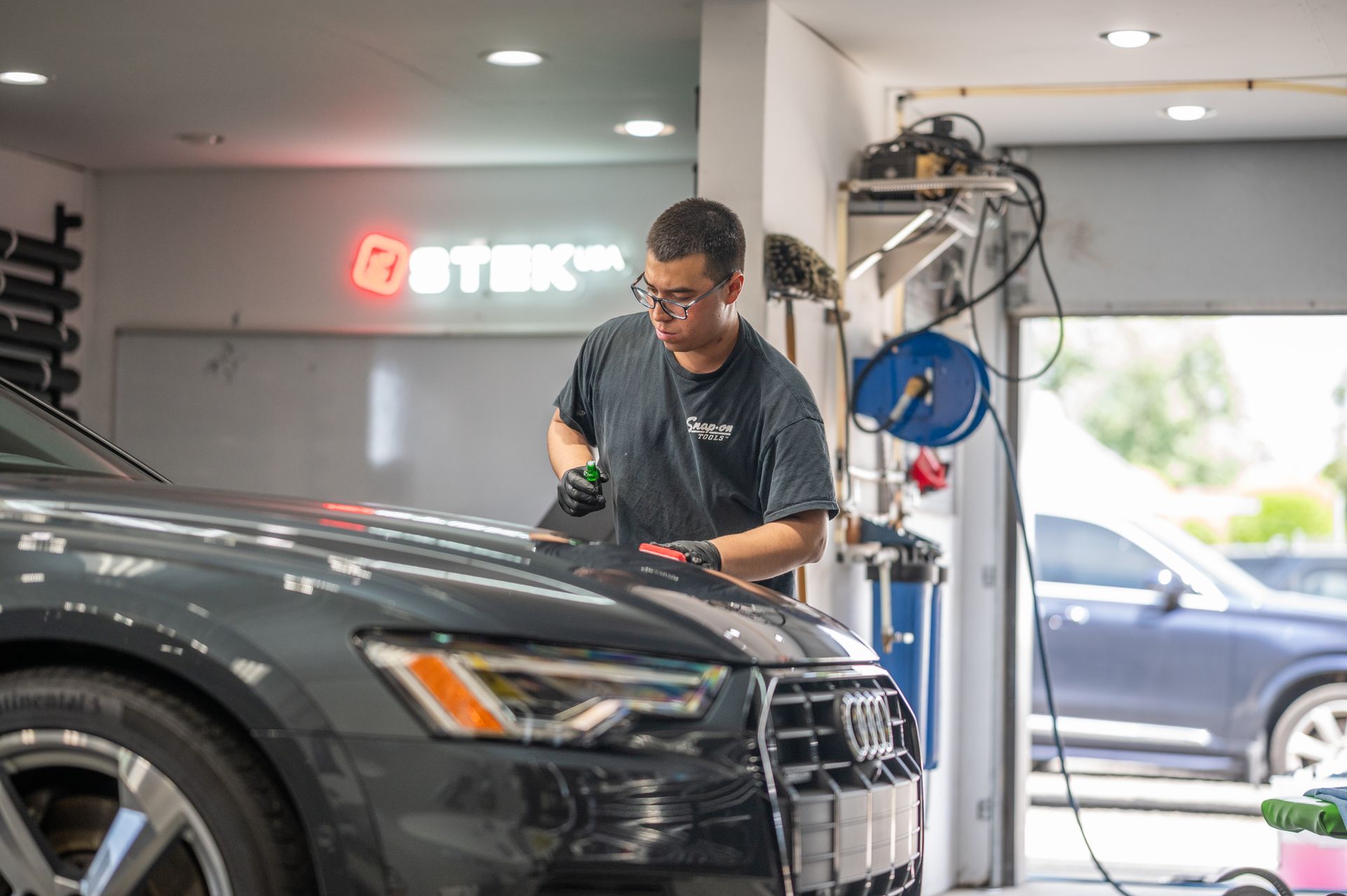 Mechanic polishing a black car in a bright auto detailing shop