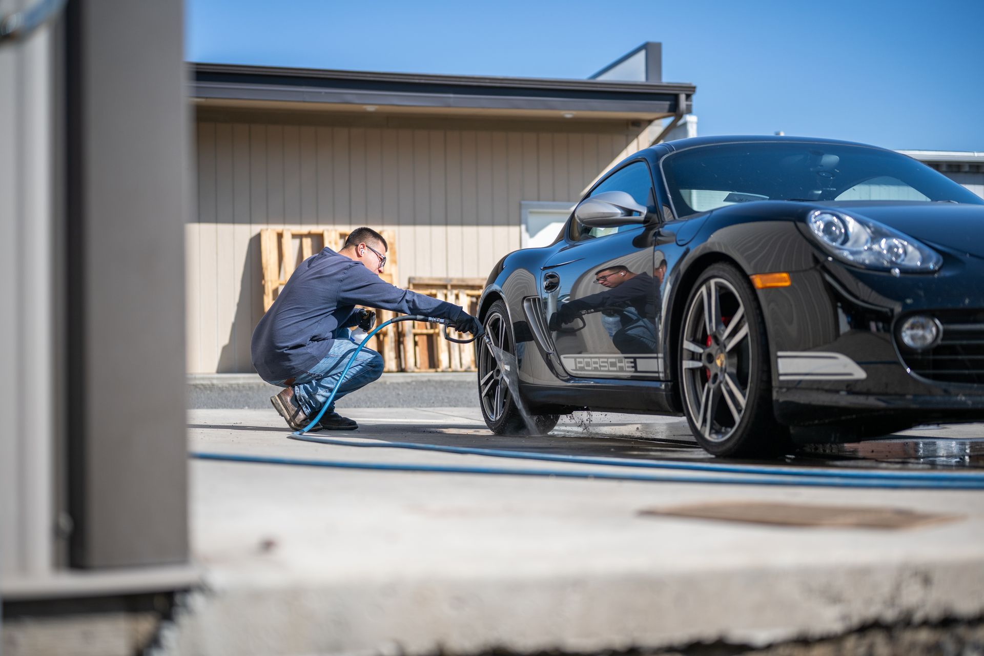 Person crouches beside a black sports car, working on a front wheel in a driveway.
