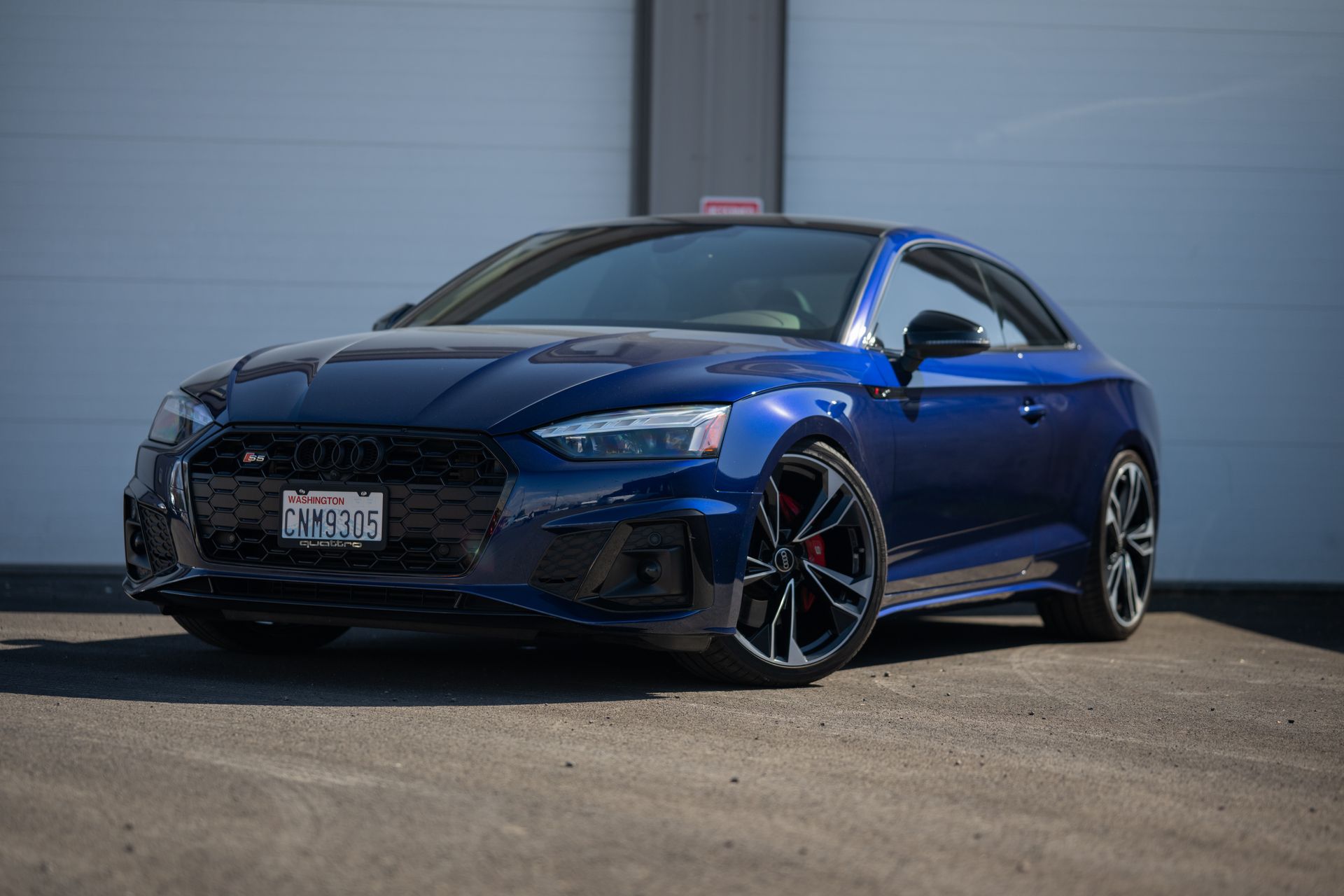 Blue sports coupe parked outdoors in front of a gray building