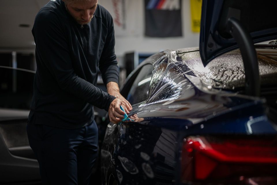 Person polishing a dark blue car in a garage, with water spraying across the rear panel