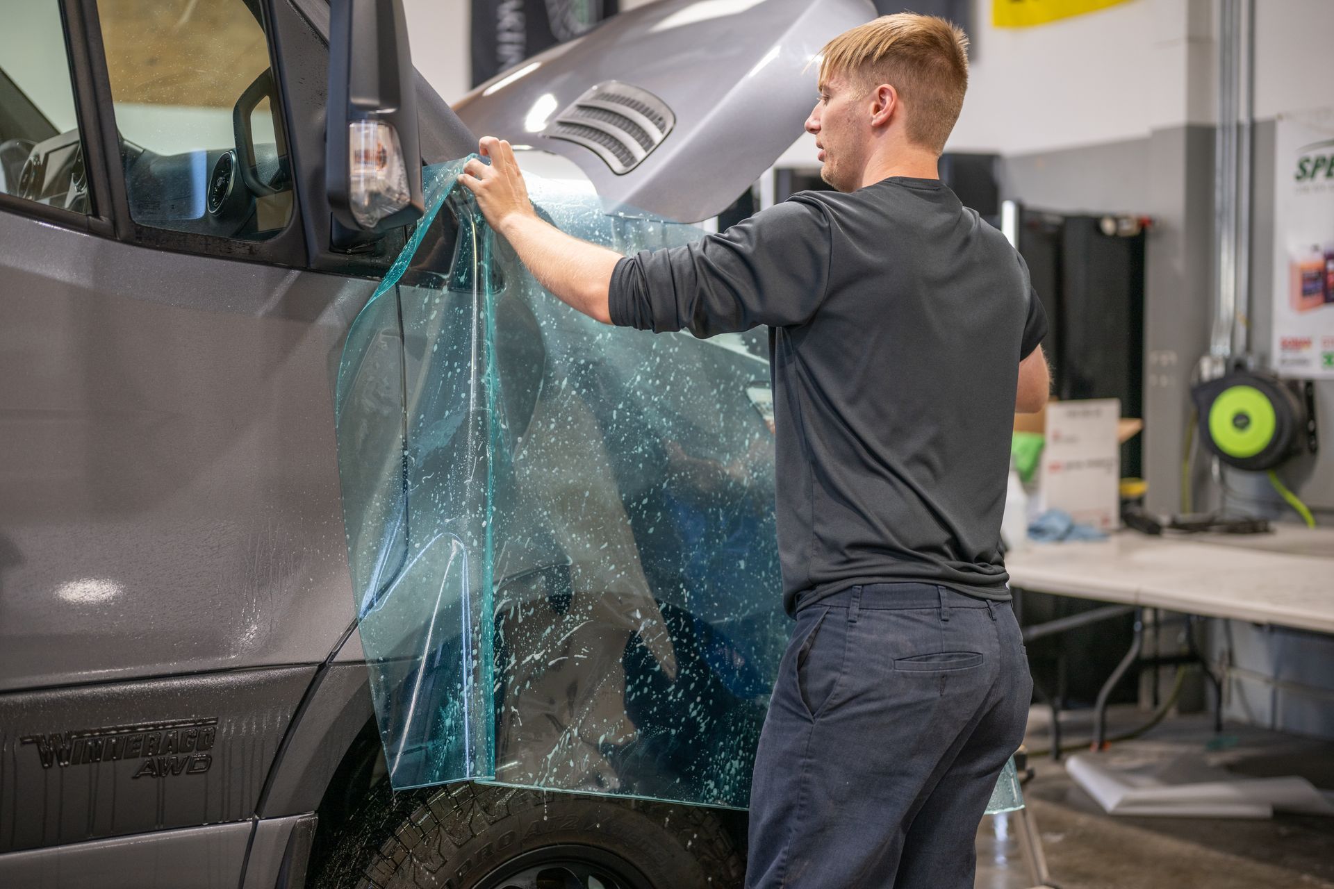 Person applying blue-tinted film to a dark vehicle in an auto shop