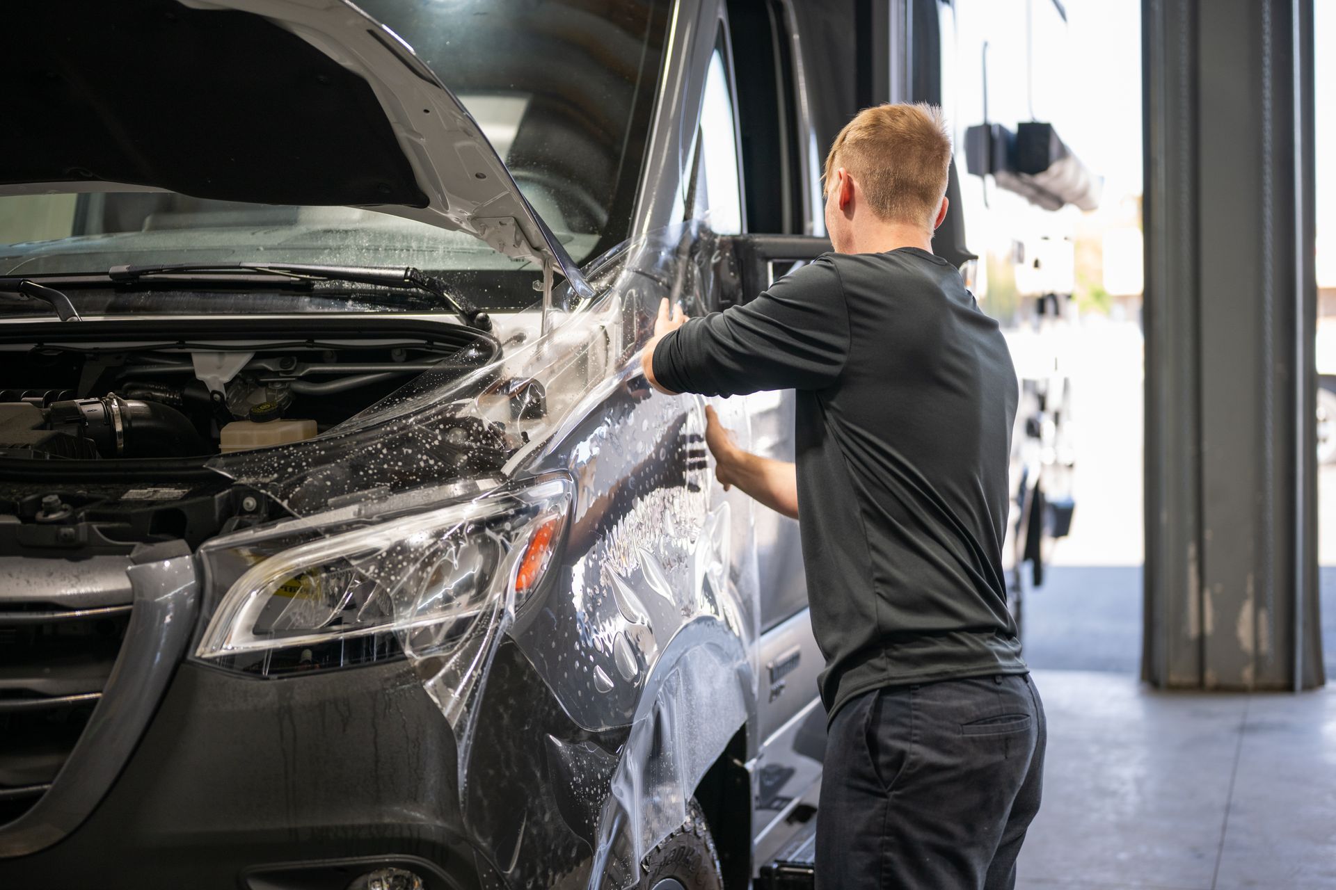Worker washing a black car with soap and water in an auto detailing bay
