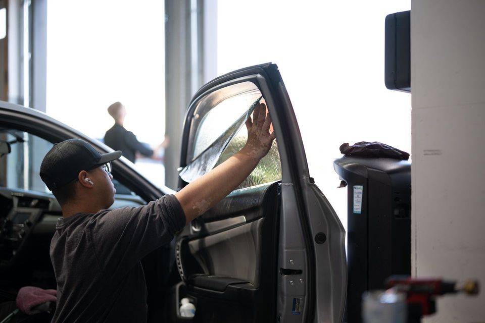 Person working on the inside of a car door in a garage, with sunlight in the background