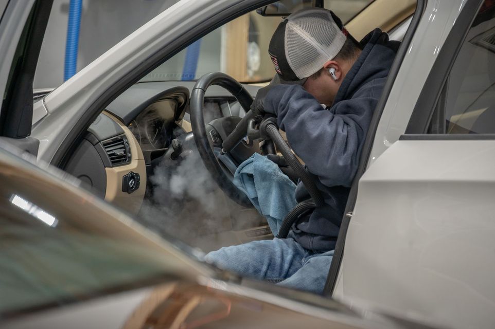Mechanic working under the dashboard of a car with smoke or steam inside the cabin