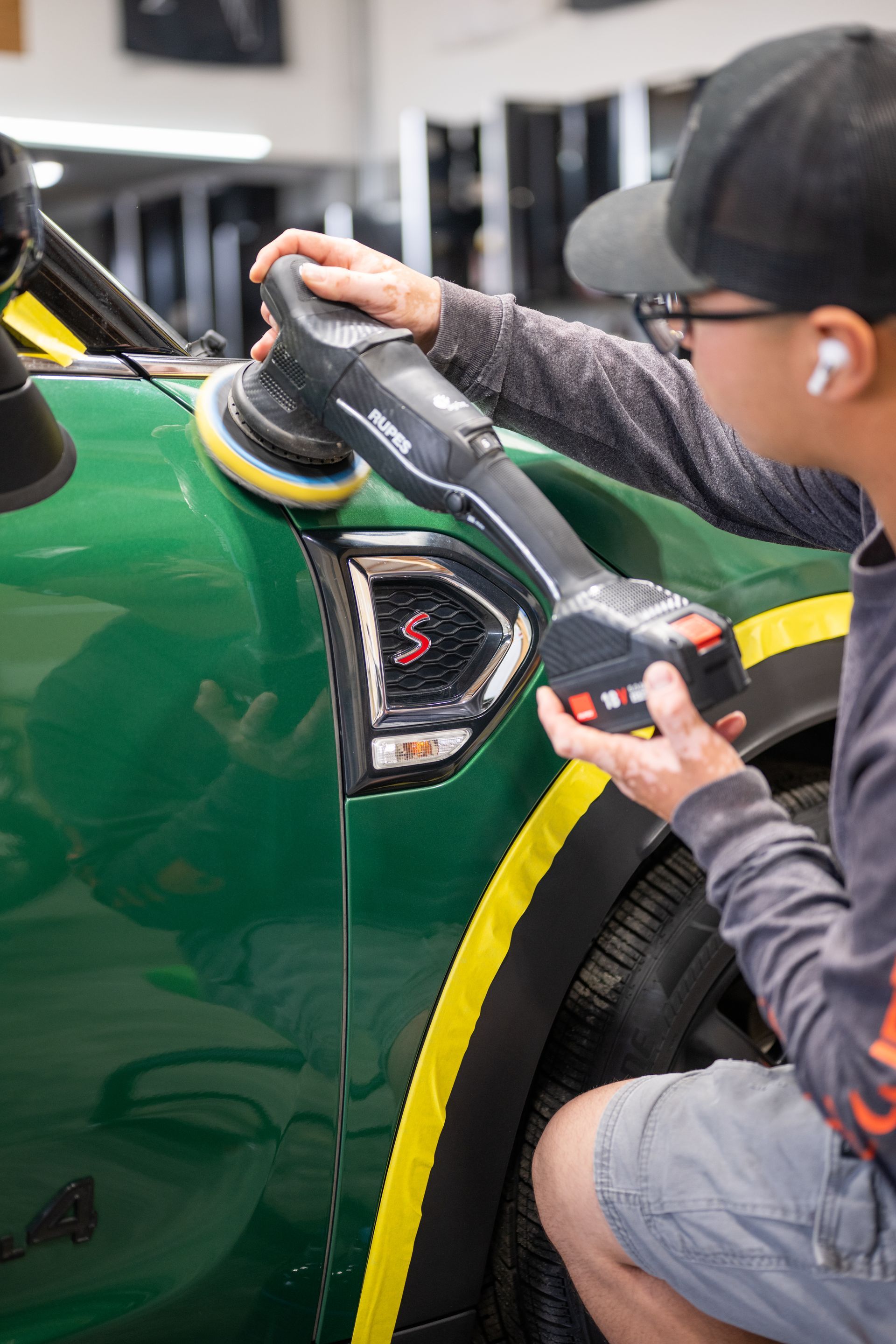 Detailing a green car with a handheld polisher, adding yellow trim along the fender seam