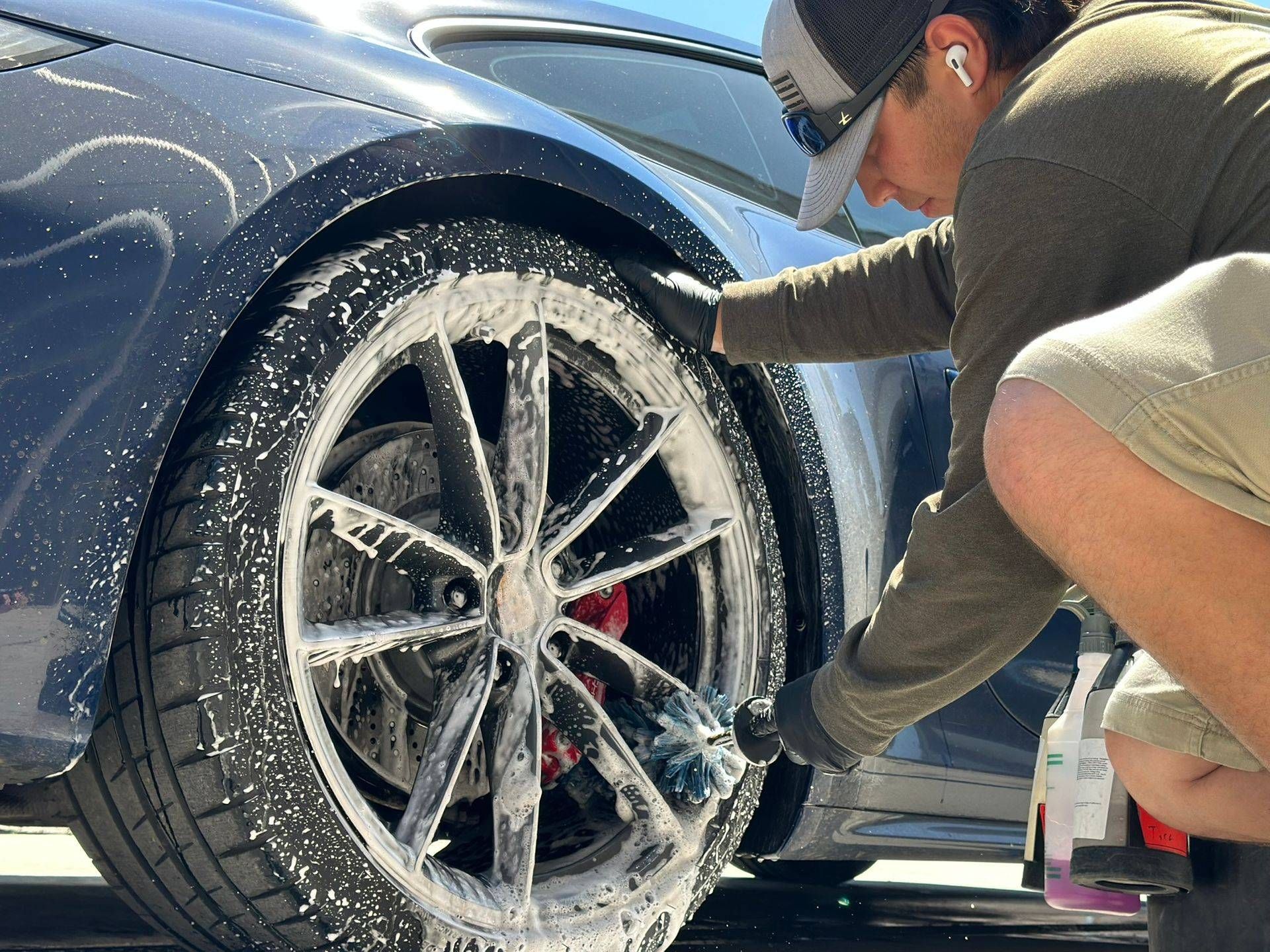 Person washing a dark blue car wheel with soap suds outdoors