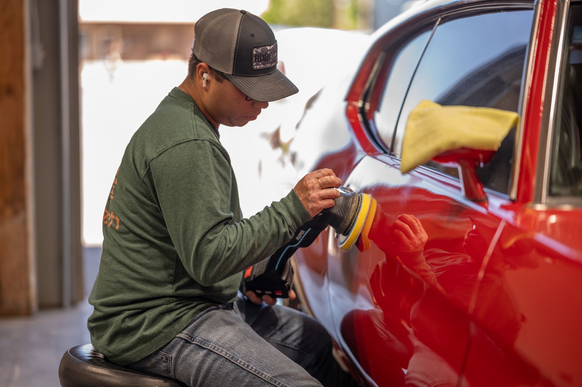 Person polishing a red car with a buffer in a garage