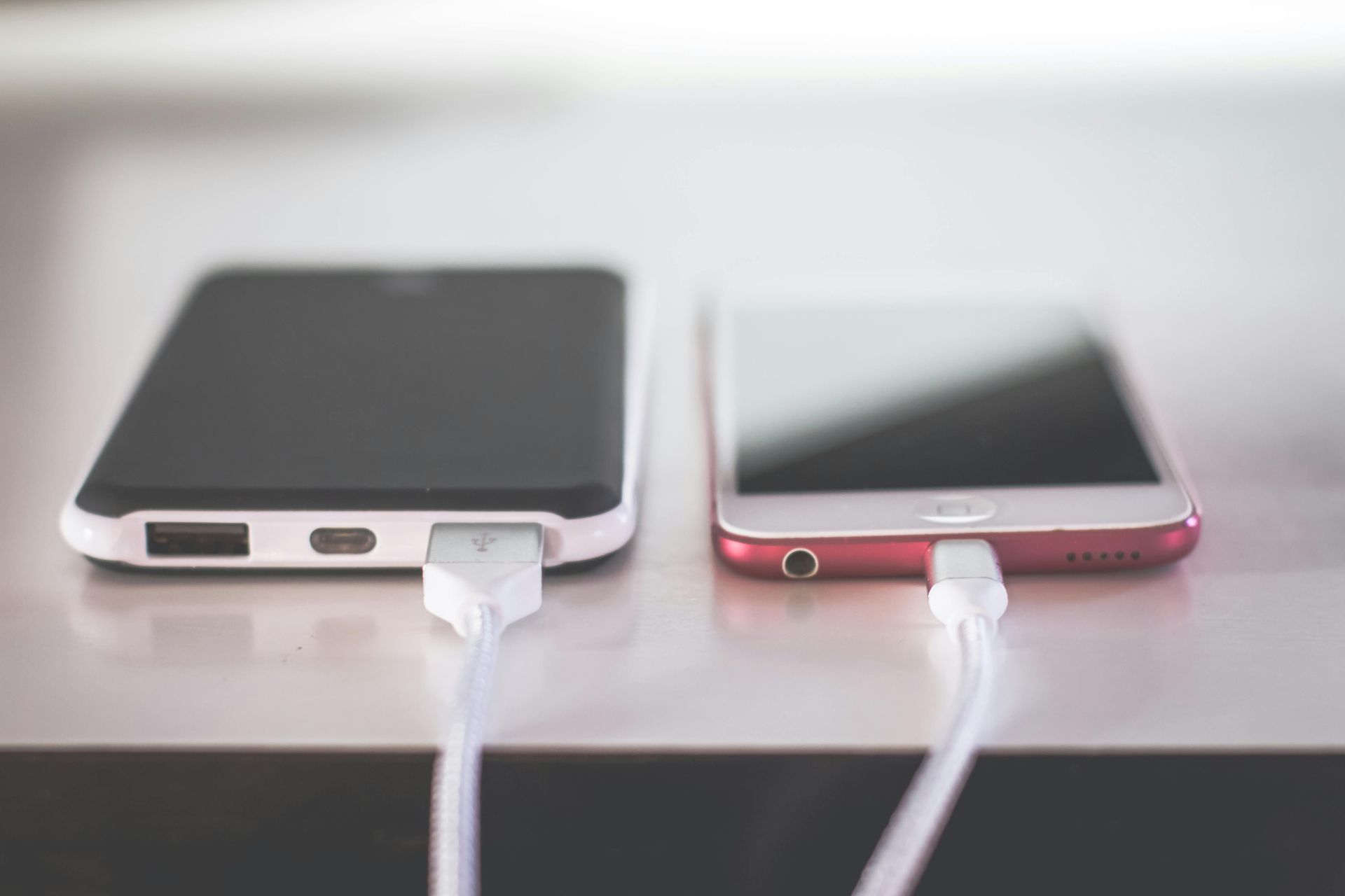 Two smartphones charging, one black, one red, connected by white cables.