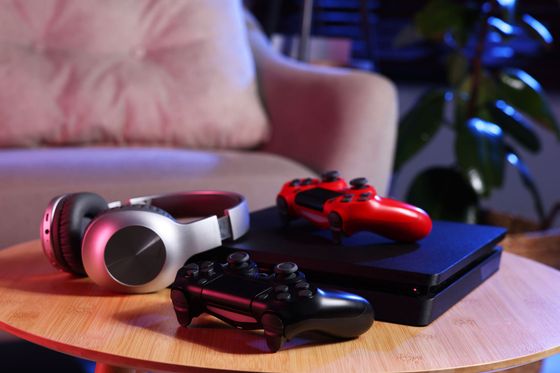 White and red headphones with two game controllers on a wooden table beside a blue console
