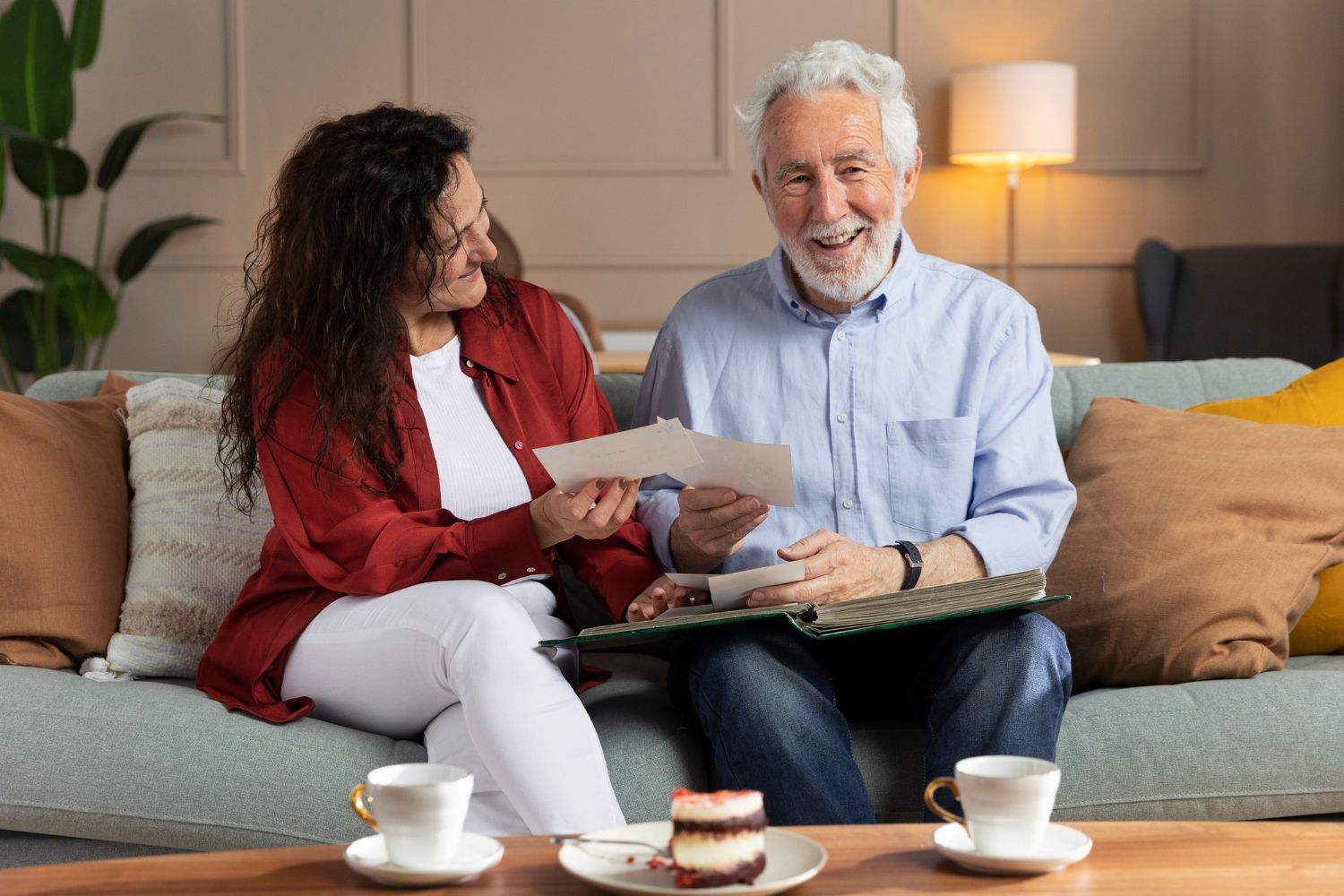 Two people chatting on a couch with tea cups and cake in a cozy living room