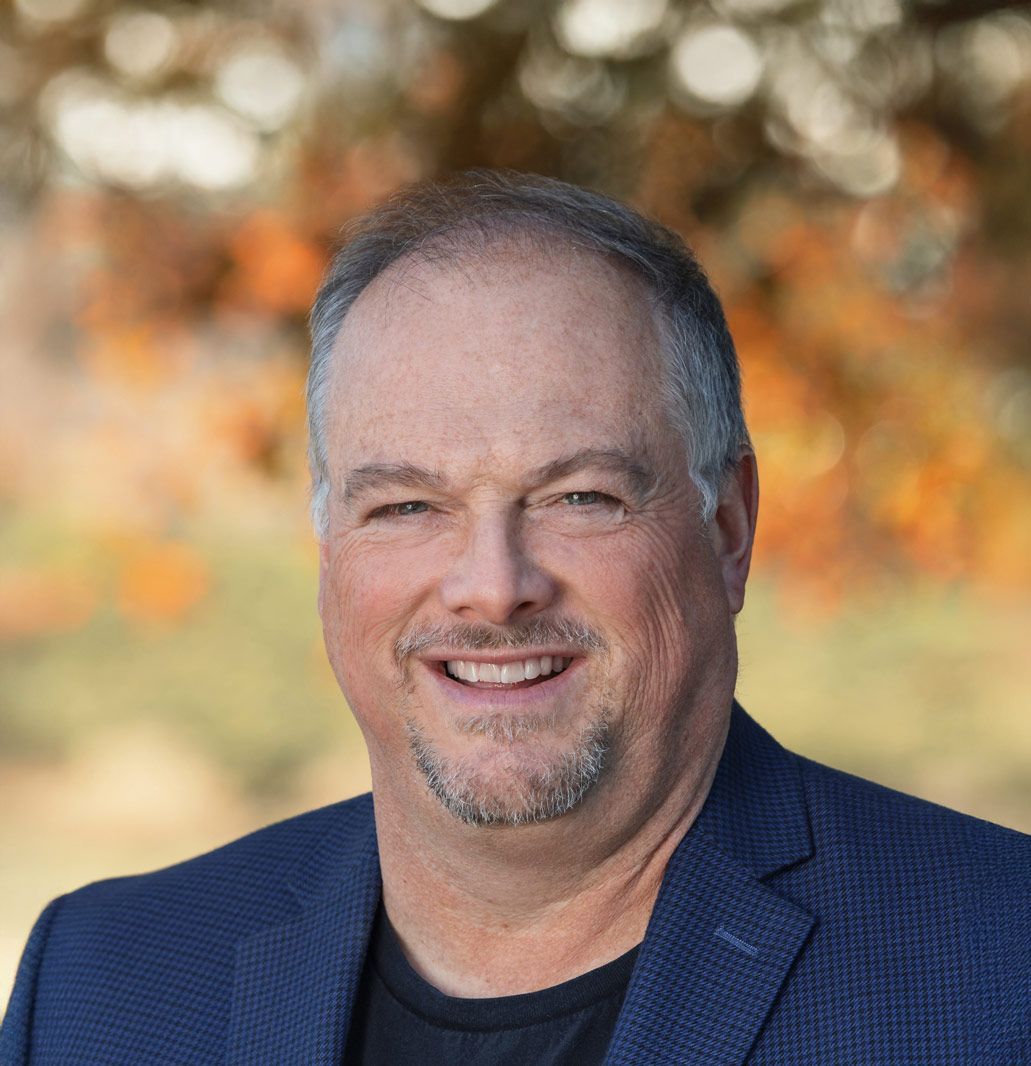 Smiling man in a navy blazer with blurred outdoor background