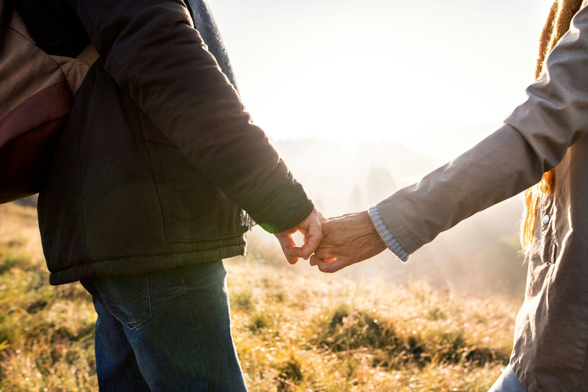Two people holding hands in a sunlit field at sunset