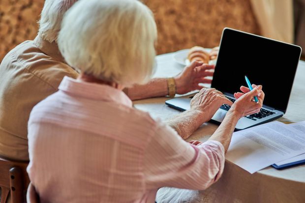 Two people at a table using a laptop and notebook, with one holding a pen.
