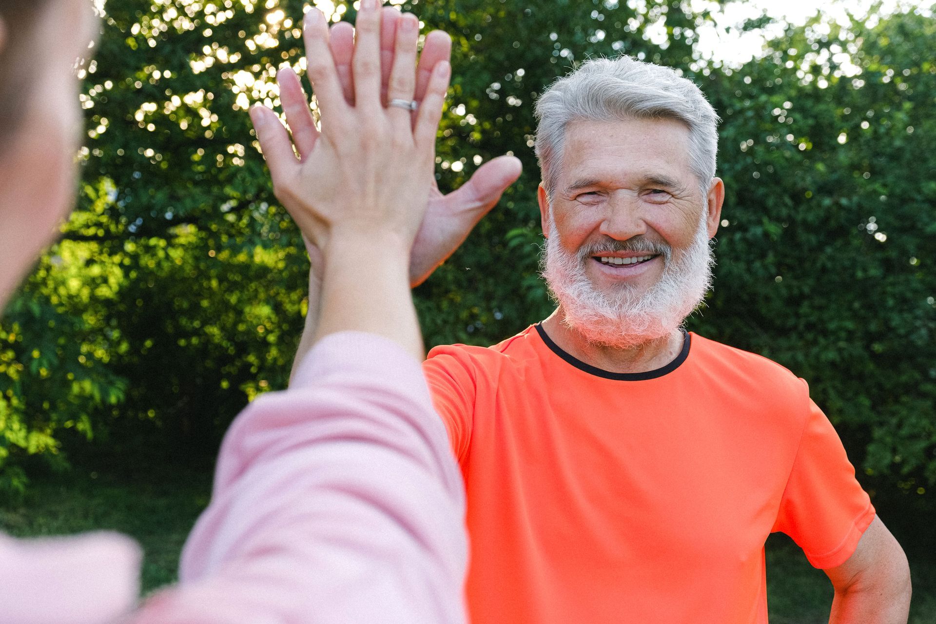 Two people high-five outdoors, with one in a bright orange shirt smiling.