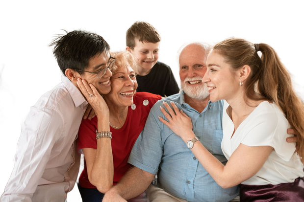 Five smiling people gathered closely together, posing and touching shoulders in a bright studio setting