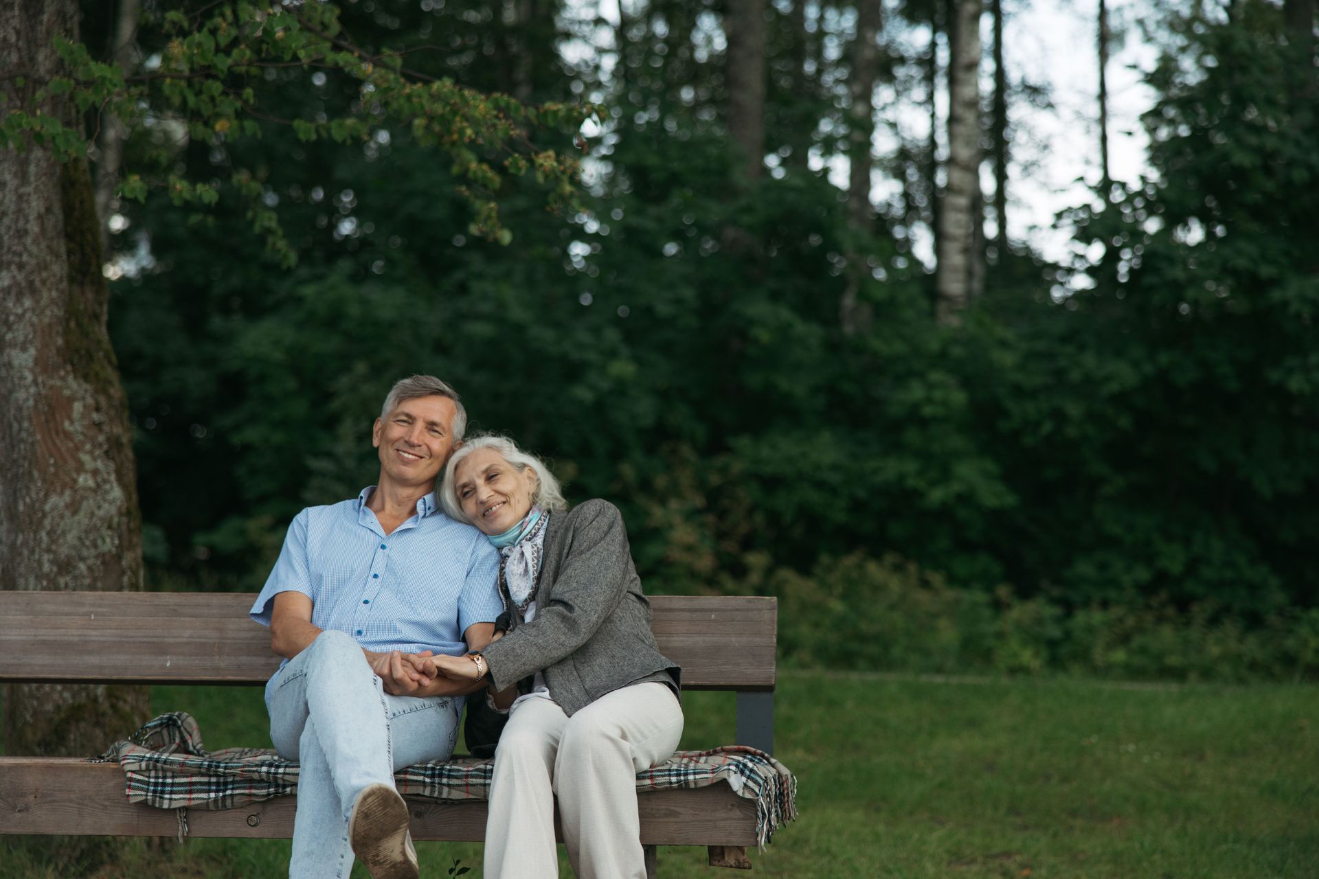 Two people sitting close together on a park bench, smiling in a green wooded area.