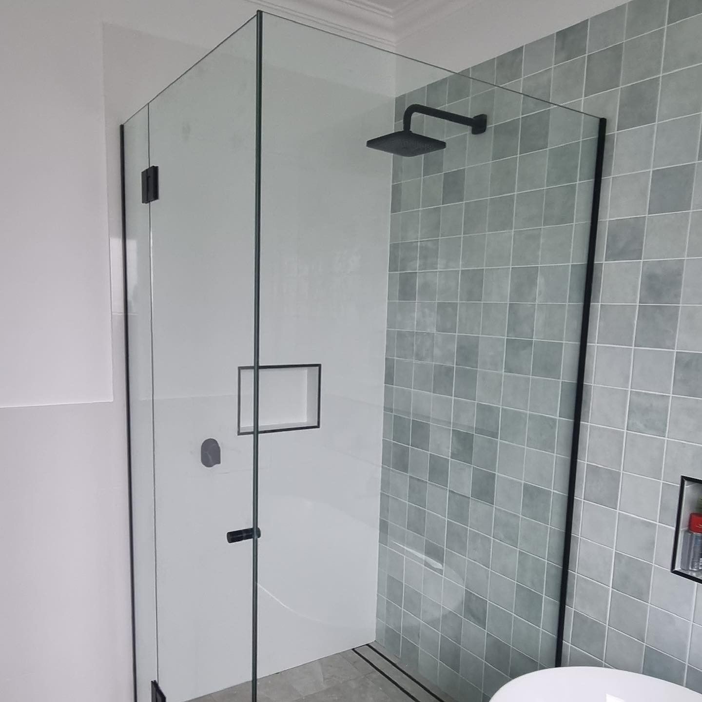Modern shower enclosure with black trim and showerhead, green tiled wall.