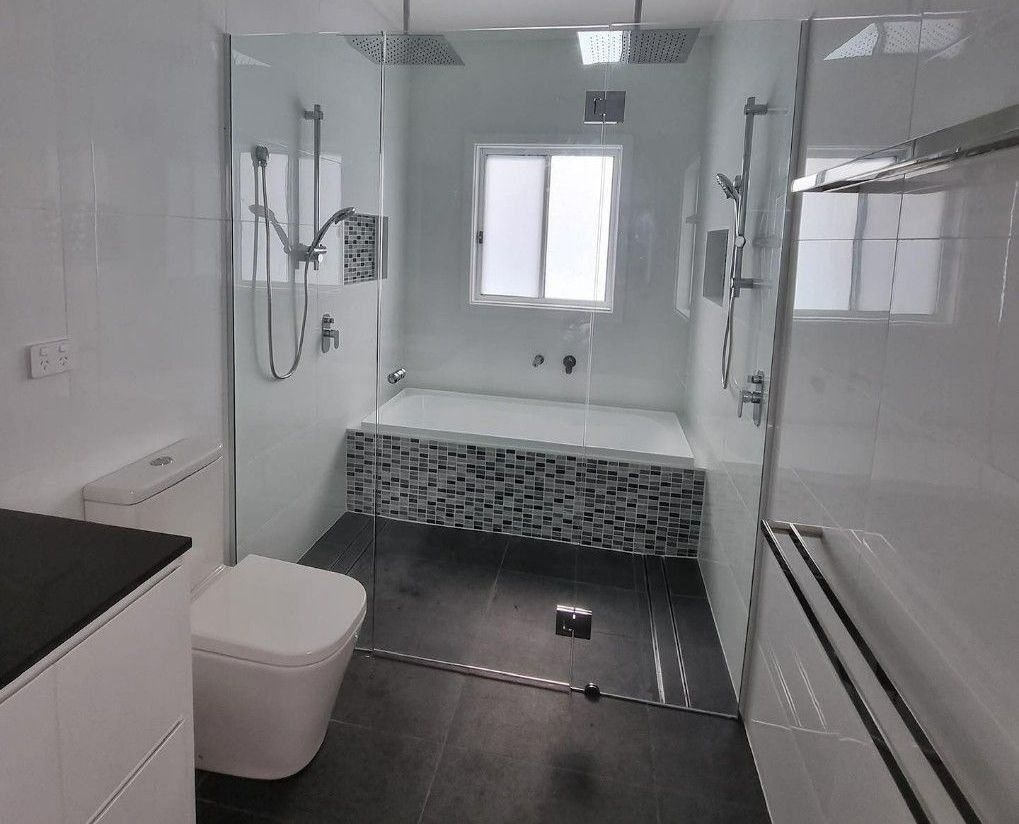 Modern bathroom with a glass-enclosed shower, built-in tub, white and black tiles, and a toilet.