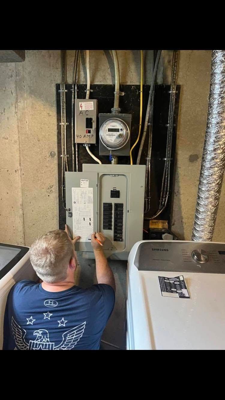 Technician installing an electrical panel in a utility room, with exposed wiring and meters above.
