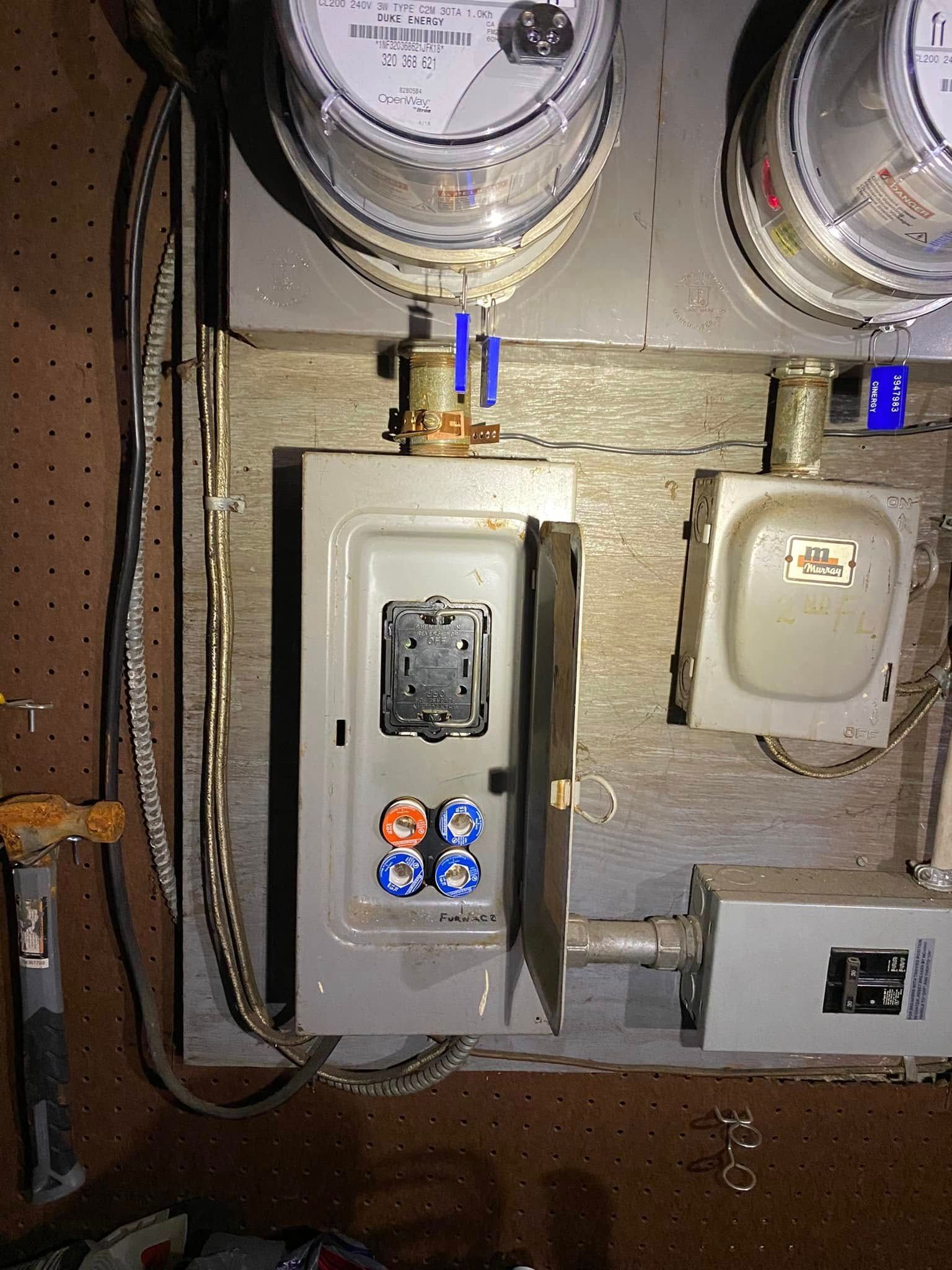 Two electric meters and breaker panels mounted on a wooden utility board