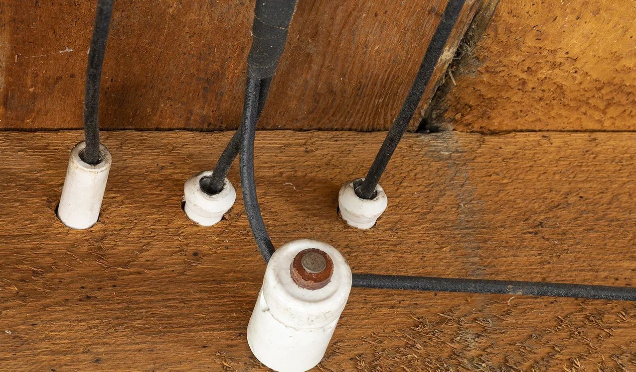 White electrical outlets and black cords on a wooden floor against a wall.