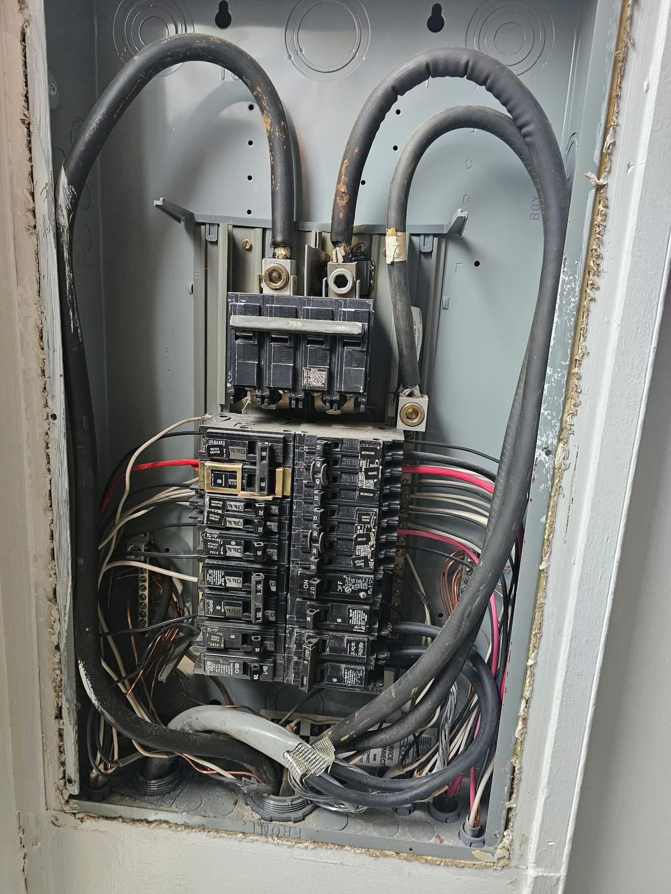 Open electrical breaker panel with wires and circuit breakers inside a gray metal box