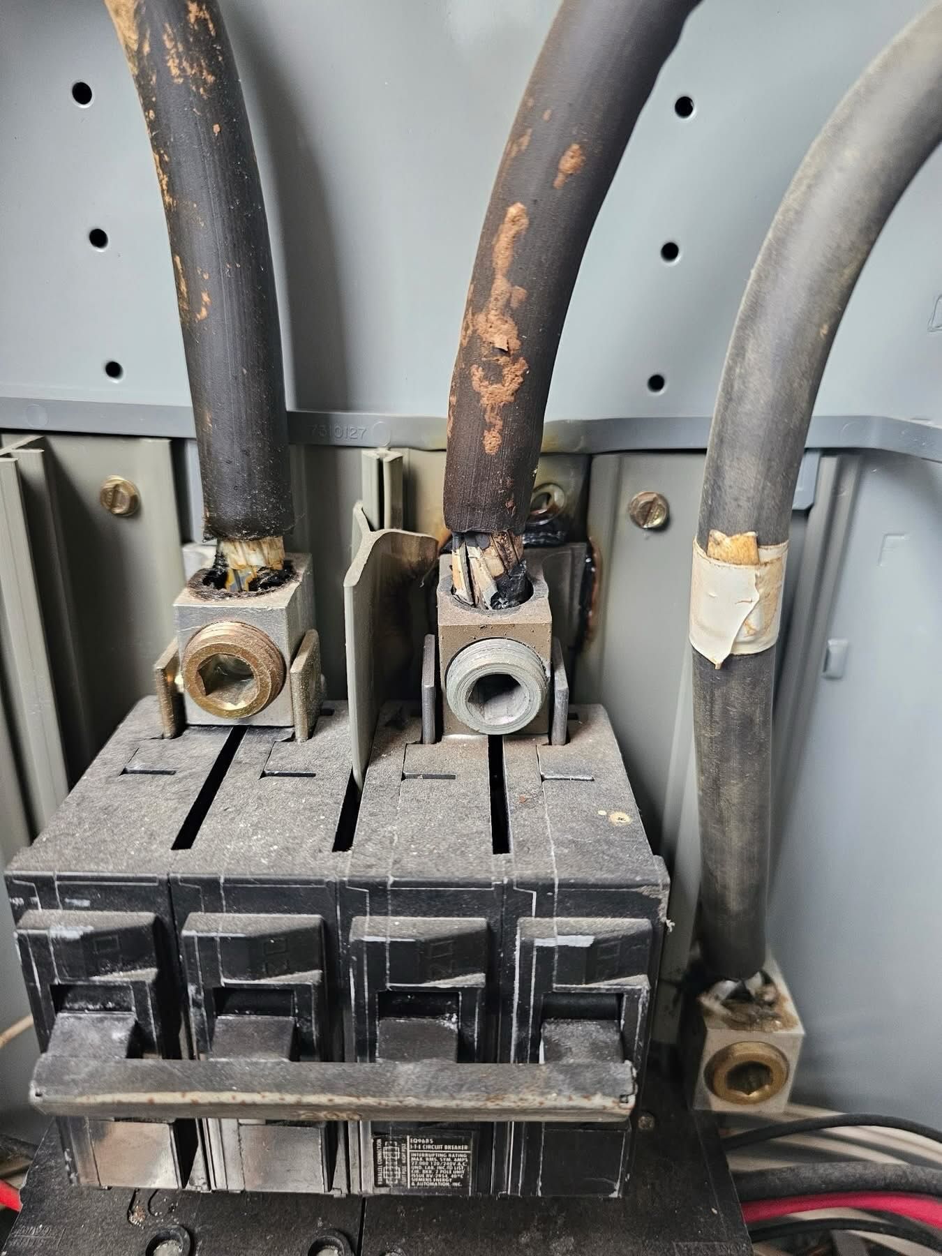 Electrical breaker panel with three thick cables and a corroded central connection point