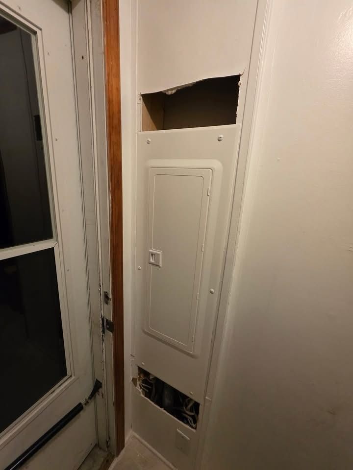 Damaged white wall panel with open access cutouts beside a window and door frame