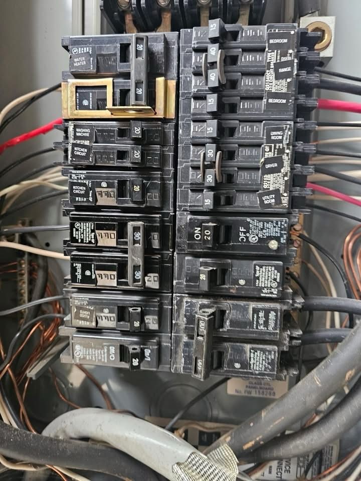 Electrical breaker panel with rows of circuit breakers and thick cables inside a utility box