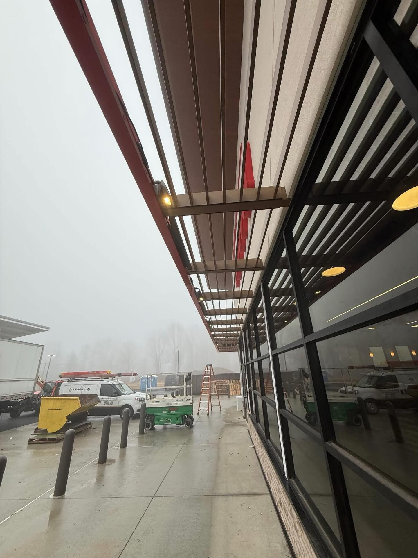 Covered sidewalk at a bus stop in rainy weather, with buses and a glass storefront on the right.