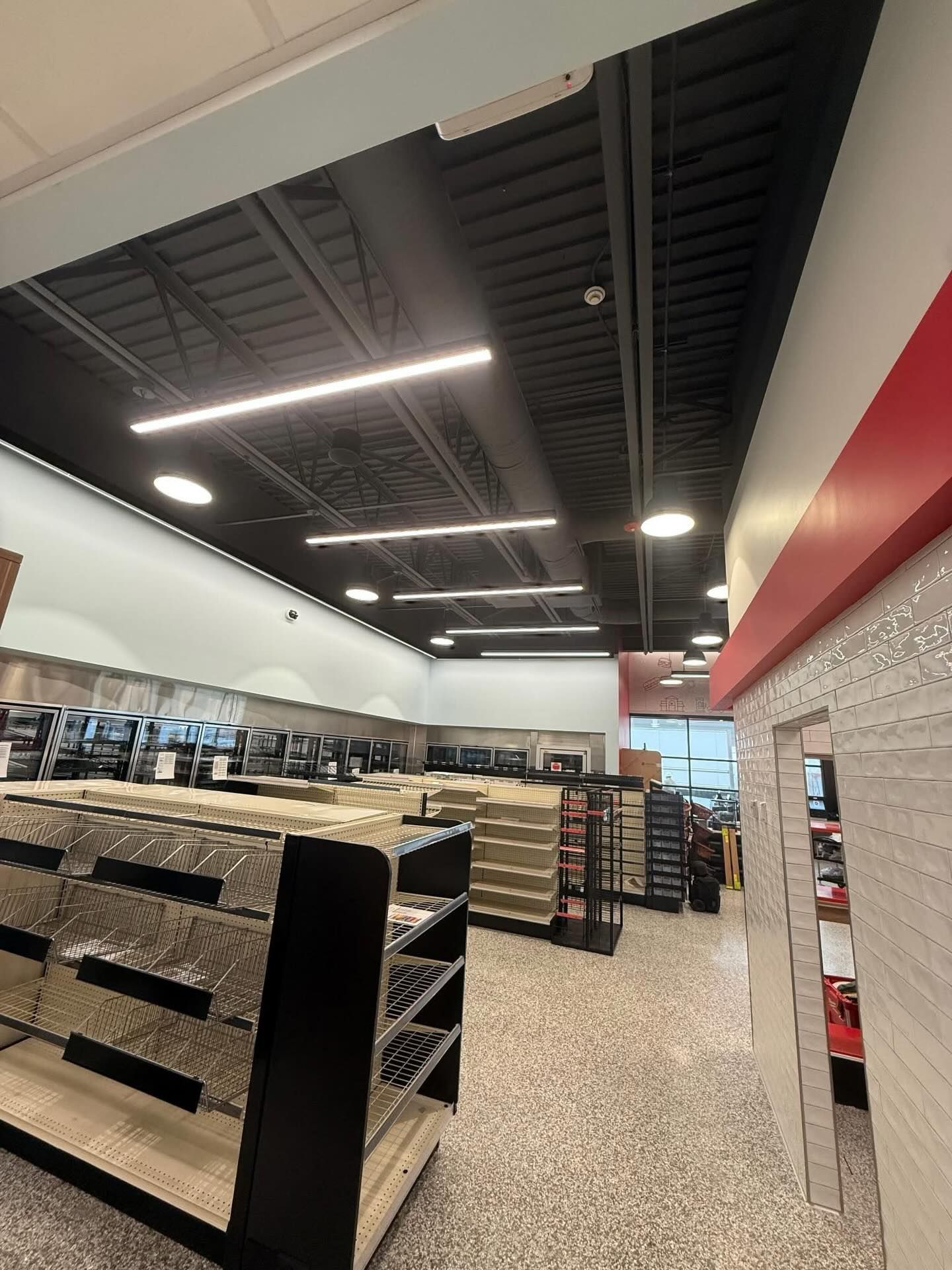 Empty convenience store aisle with shelves, black ceiling, and bright overhead lights.