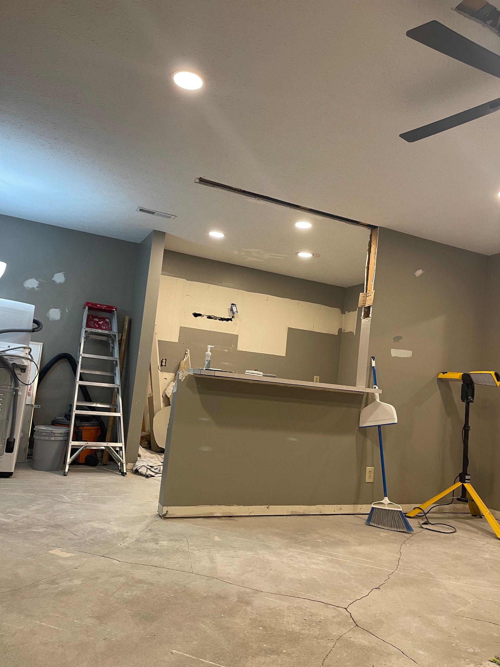 Unfinished basement with concrete floor, kitchen island, ladder, and tools under recessed lights