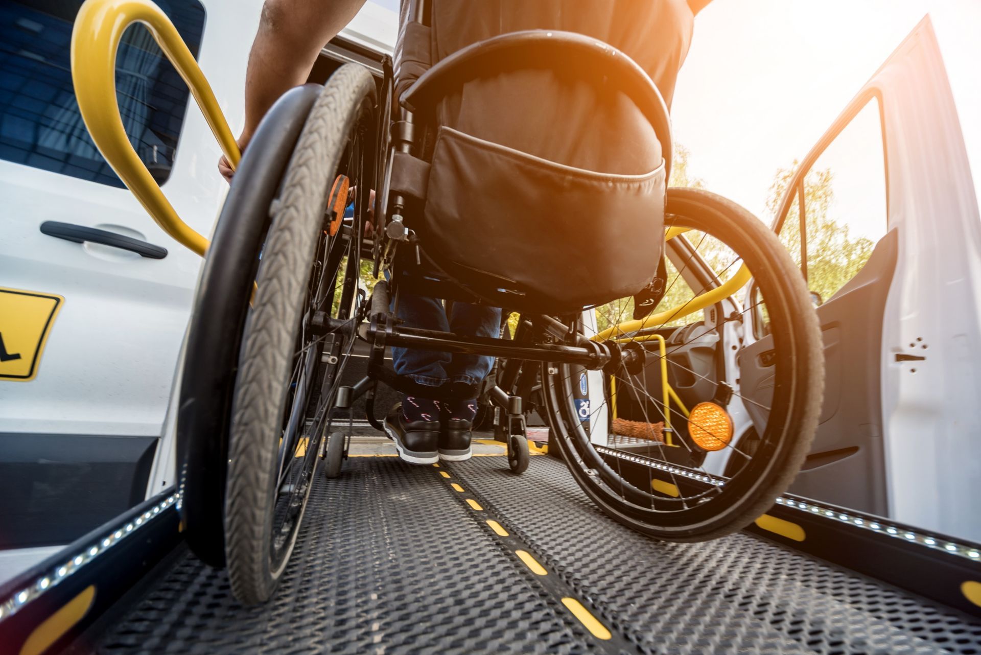Wheelchair ramp on a van, with a person rolling up a textured metal lift in bright sunlight
