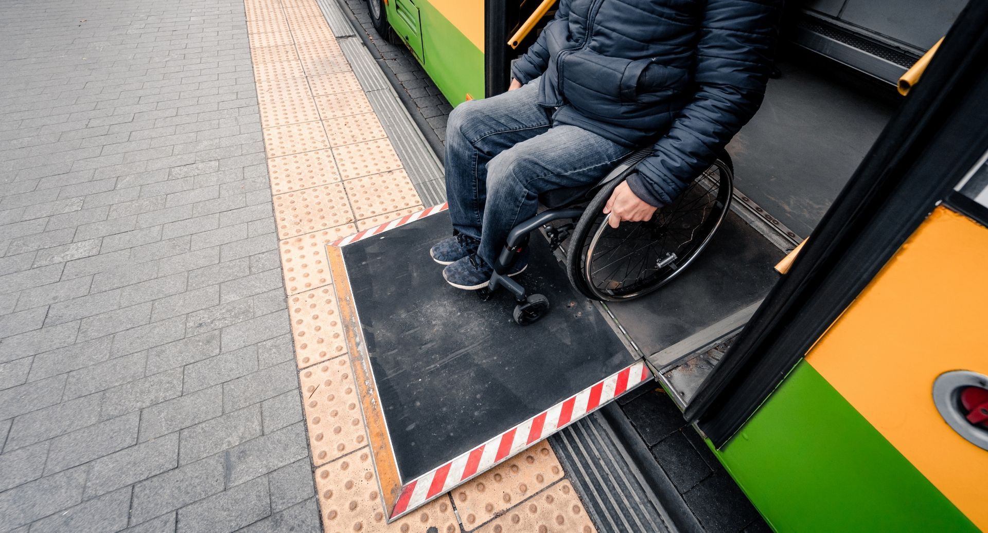 Person in a wheelchair boarding a green and yellow bus via a ramp at the door.