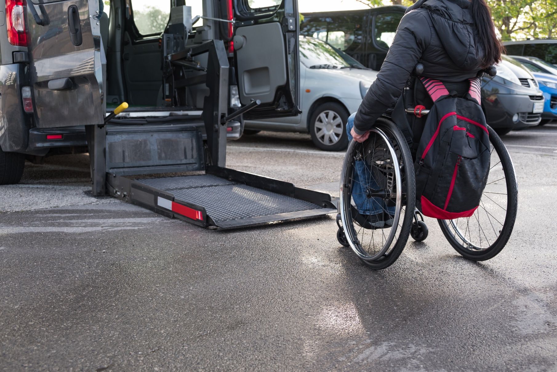Person in a wheelchair boarding a van using a ramp on a wet street.