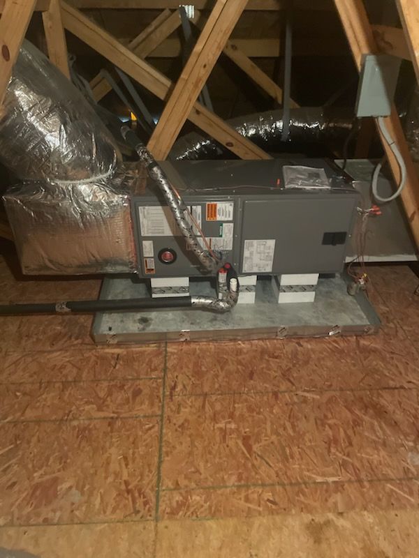 HVAC unit in an attic with ductwork, wooden beams, and a plywood floor.