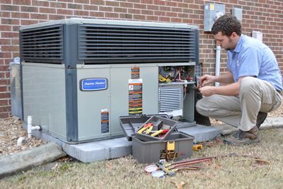 HVAC technician repairs an air conditioning unit outside a brick building.