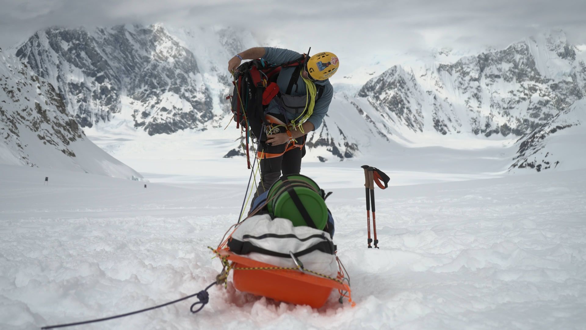 Mountaineer in snowy mountains, preparing gear near a sled.