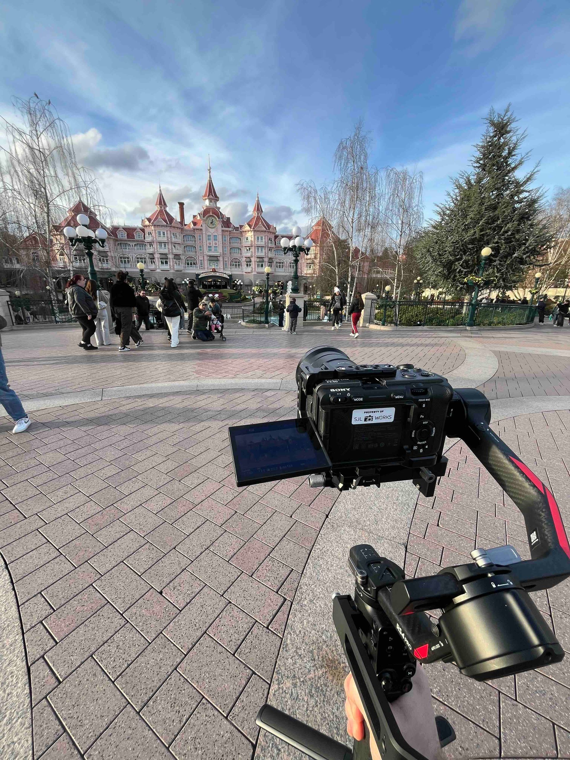 Camera on a gimbal pointed at Disneyland castle with people milling about. Blue sky.