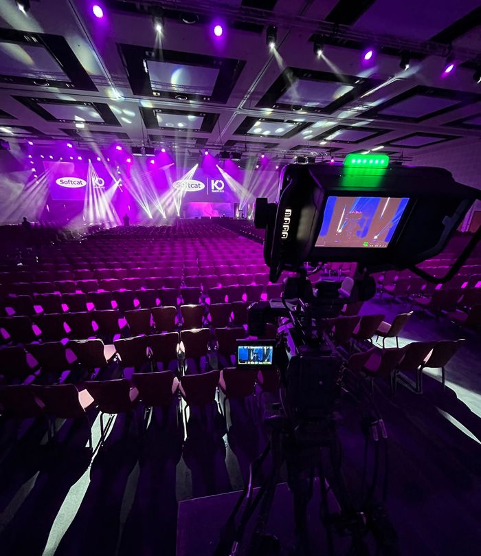 Purple-lit conference hall with empty rows of seats and stage lights illuminating the room