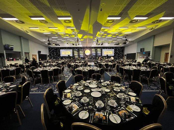 Banquet hall with round tables set for a formal event, stage at the front, and yellow ceiling lighting