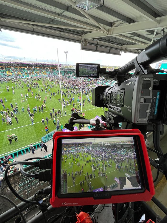 TV camera view over a crowded stadium field during a soccer match, with monitors in the foreground