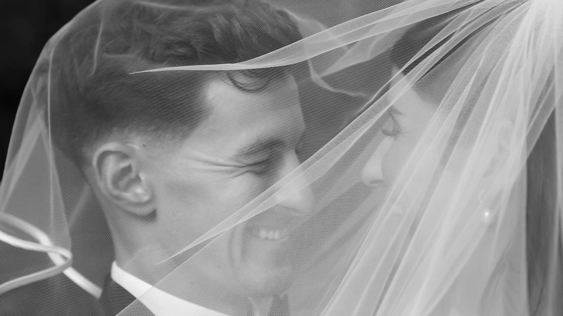 Man smiling, face partially obscured by a sheer veil, likely at a wedding ceremony.