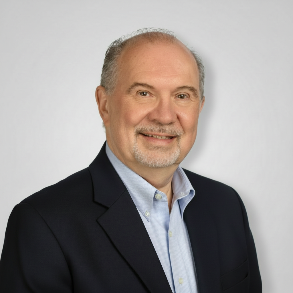 Studio headshot of a smiling man in a dark blazer and light blue shirt against a gray background