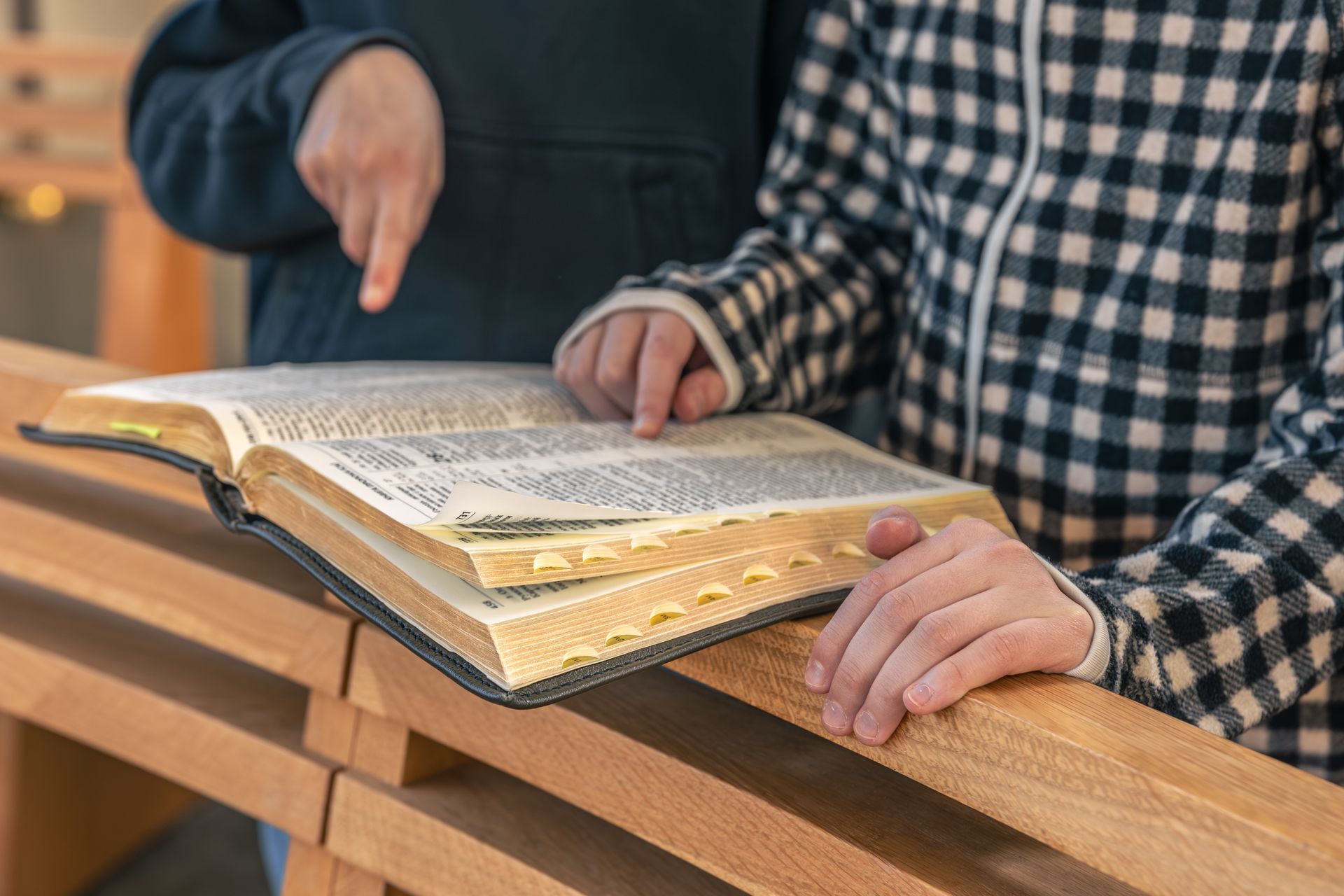 Hands pointing at an open book on a wooden desk, with one person holding the pages.