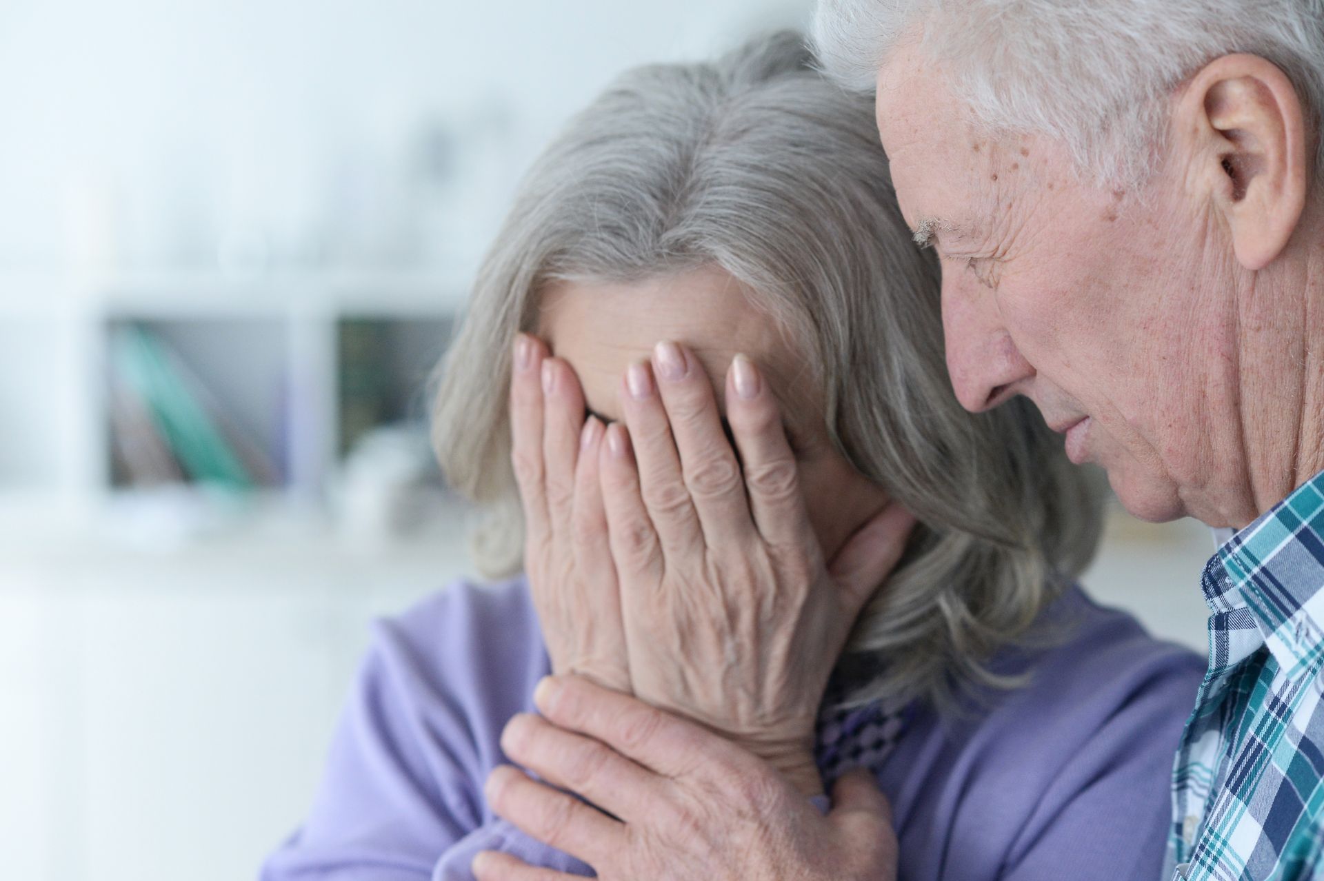 An elderly couple is sitting next to each other and the woman is covering her face with her hands.