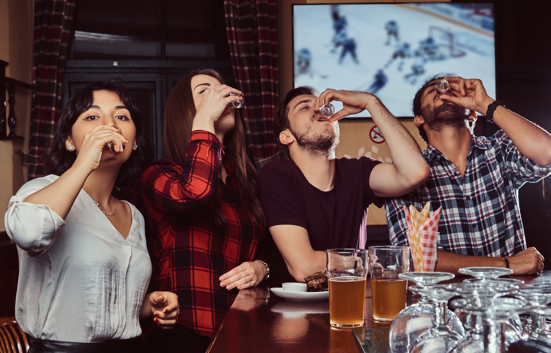 A group of people are drinking beer in a bar while watching a hockey game.