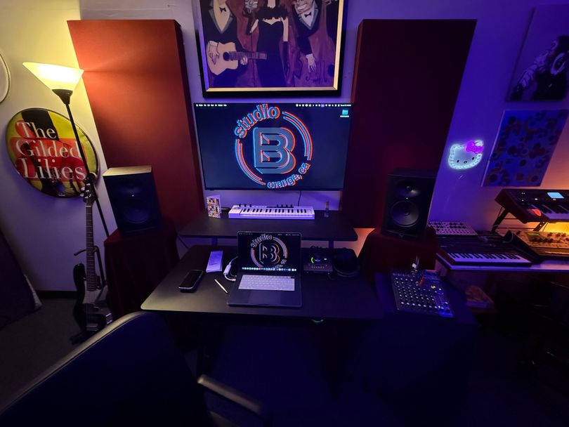 RGB-lit gaming desk setup with dual monitors, speakers, keyboard, mouse, and wall art